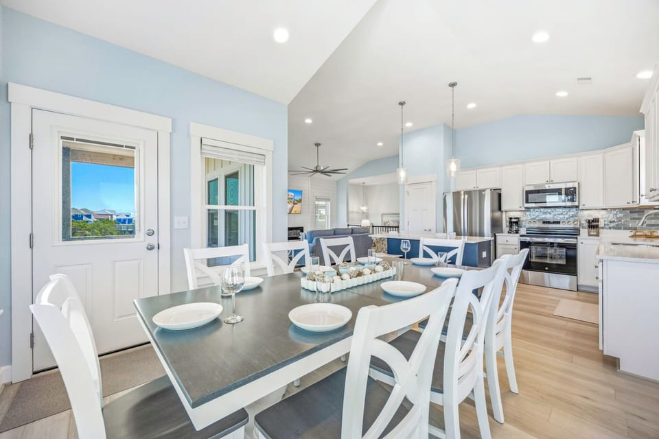 Gather around the elegant dining table where meals become cherished memories. The open-concept layout seamlessly connects you to the chef-ready kitchen, while soft blue tones and abundant natural light create a welcoming atmosphere for your vacation feasts