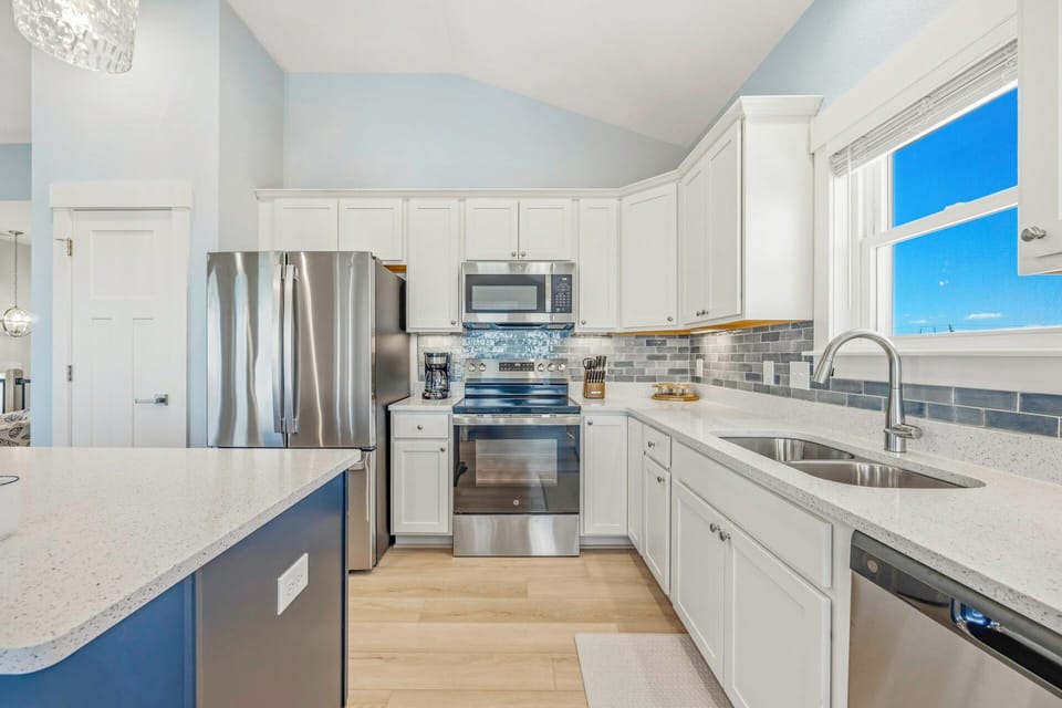 Step into your fully equipped gourmet kitchen, where stainless steel appliances, white cabinetry, and elegant countertops invite you to prepare delicious meals with natural light streaming through the window.