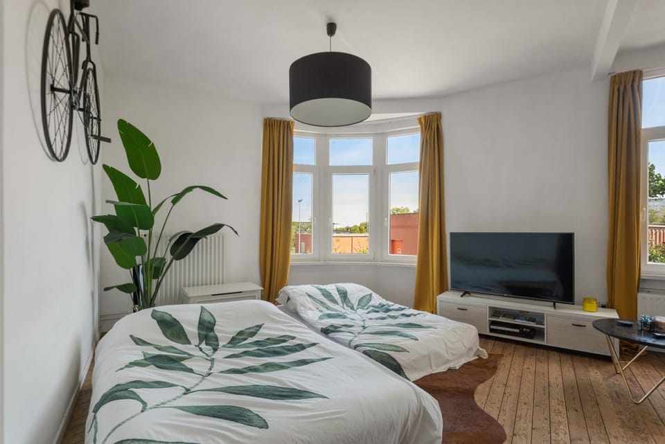 Bright sleeping area with two comfortable beds positioned near large windows that fill the room with natural light. Relax with open views outside while enjoying a simple and airy space designed for a restful stay.