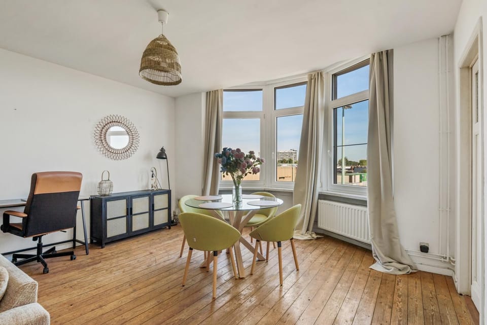 Dining area set beside large windows that fill the space with natural light and open views of the neighborhood. A round table with comfortable chairs creates a pleasant spot for meals, morning coffee, or quiet work during the day.