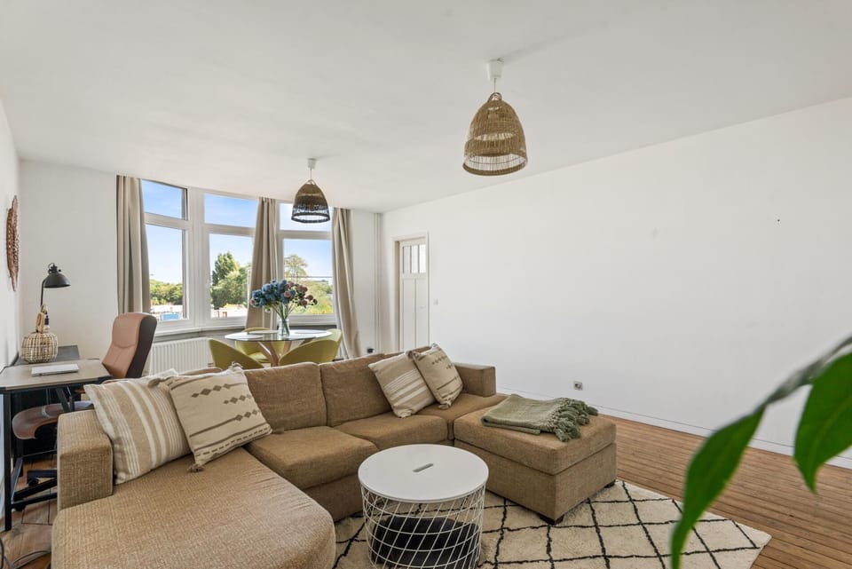 Bright open living area with a comfortable sectional sofa and large windows that fill the space with natural light. The room connects to a cozy dining corner, creating a relaxed setting for lounging, working, or gathering after a day out.