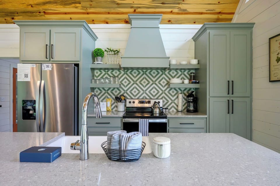 Step into your gourmet kitchen where sage cabinets and geometric backsplash create culinary magic beneath warm wood beams.