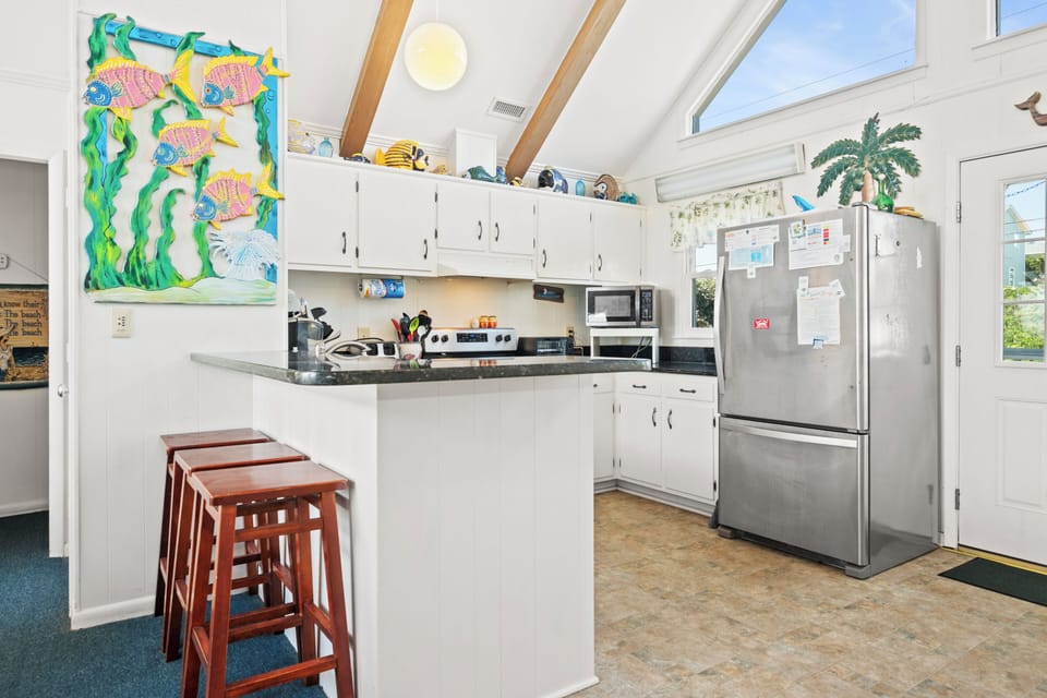 Gather around the bright kitchen island with stainless appliances, white cabinetry, and beach-themed charm—perfect for prepping meals and planning your coastal adventures.