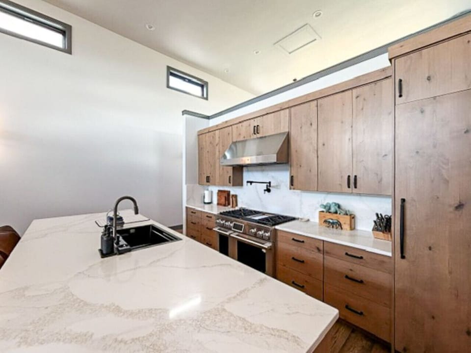 Sleek kitchen with quartz island, natural wood cabinets, and airy high‑ceiling windows
