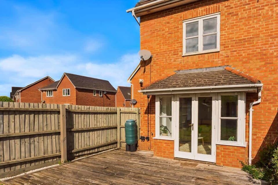 Sunny backyard with deck, fencing, and charming brick exterior.
