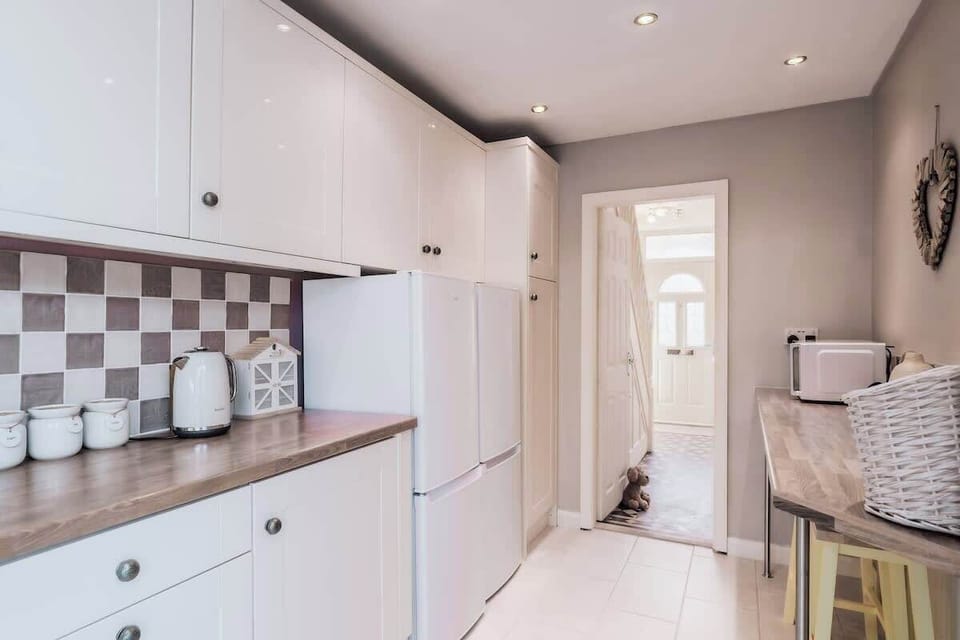 Compact kitchen hallway with white cabinets, sleek appliances, neutral tones.
