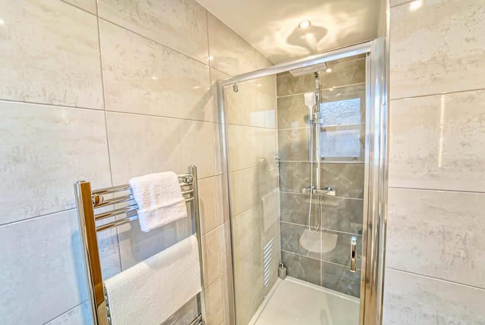 Spacious glass shower enclosure tiled walls chrome fixtures bright finish