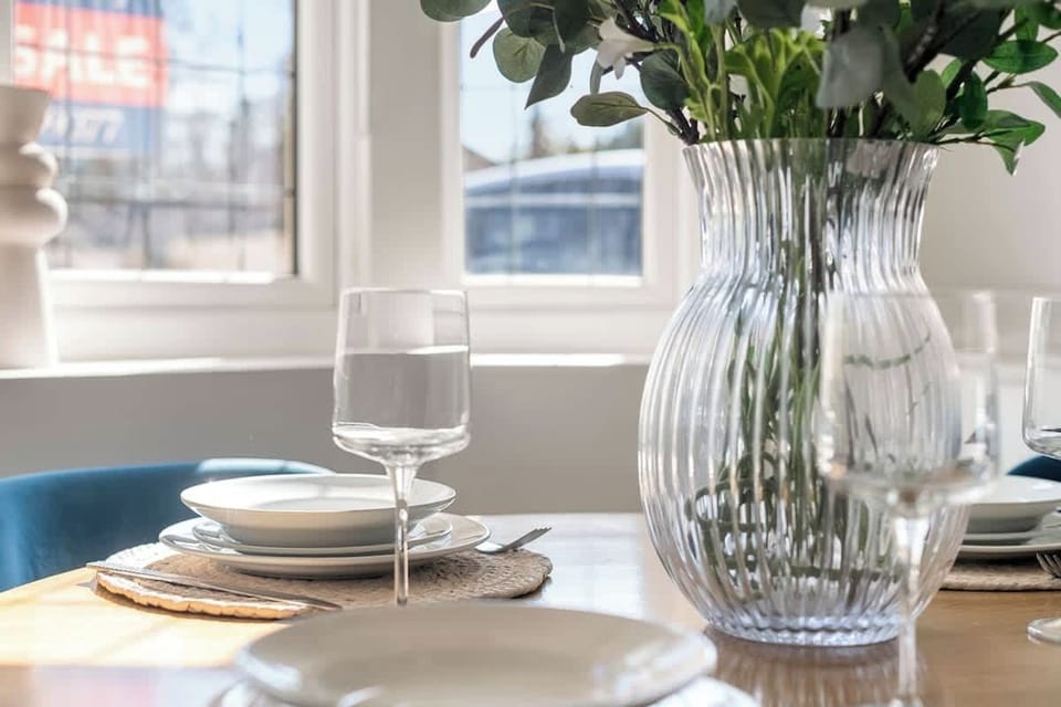 Simple dining setup with vase, glassware, and bright window backdrop.