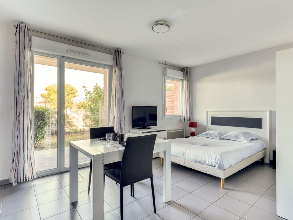 Double bed, dining area, and flat-screen TV in an open layout with sliding doors to the terrace