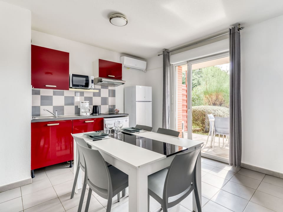 Red kitchenette with ceramic hob, microwave, and dishwasher — dining area right alongside