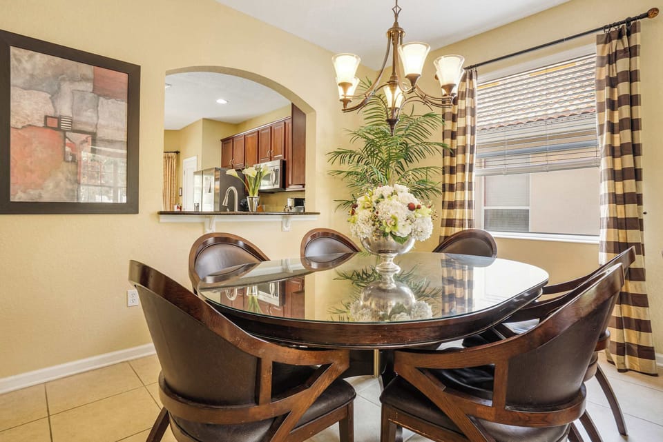 Dining area with a glass-top table and striped curtains next to the kitchen pass-through.