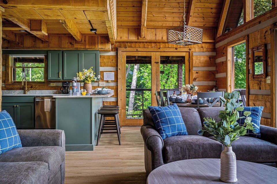 Sage-green cabinets, a gold faucet, and a breakfast bar built for slow pancake mornings — the open-plan kitchen flows straight to a dining table set for the whole crew.