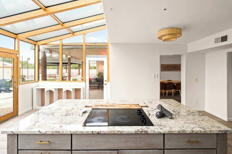 This stunning kitchen island, crowned with luxurious granite countertops and a sleek built-in cooktop, sits beneath a breathtaking glass ceiling that floods the space with natural light, creating the perfect centerpiece for cooking and gathering.