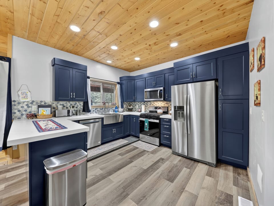 Step into your fully equipped modern kitchen with rich navy cabinetry, stainless appliances, and warm wood plank ceilings—your home base for meals and memories.