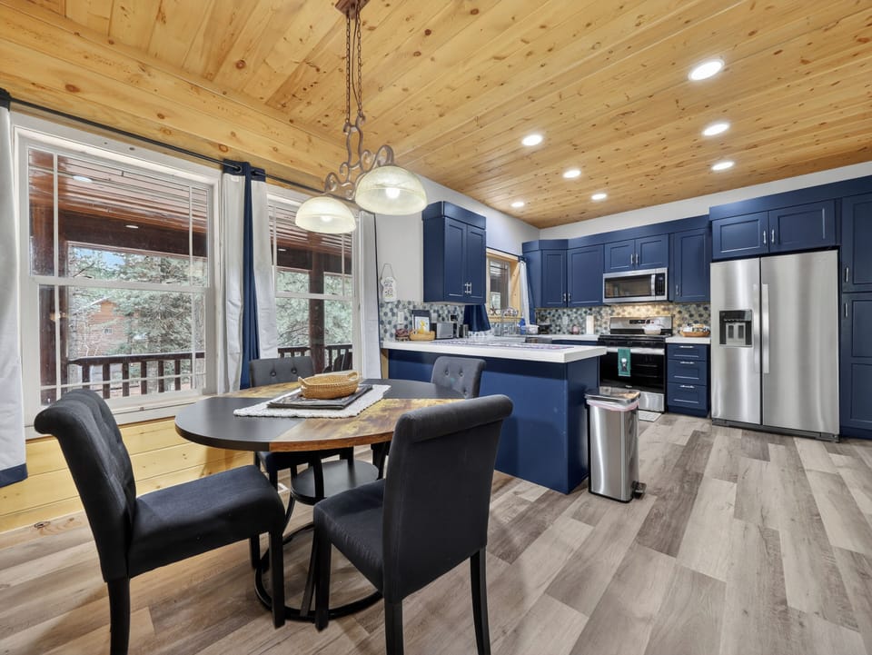 Picture yourself cooking in this stunning kitchen with navy cabinetry, stainless steel appliances, and warm pine ceilings. Dine at your cozy table as natural light streams through the windows.