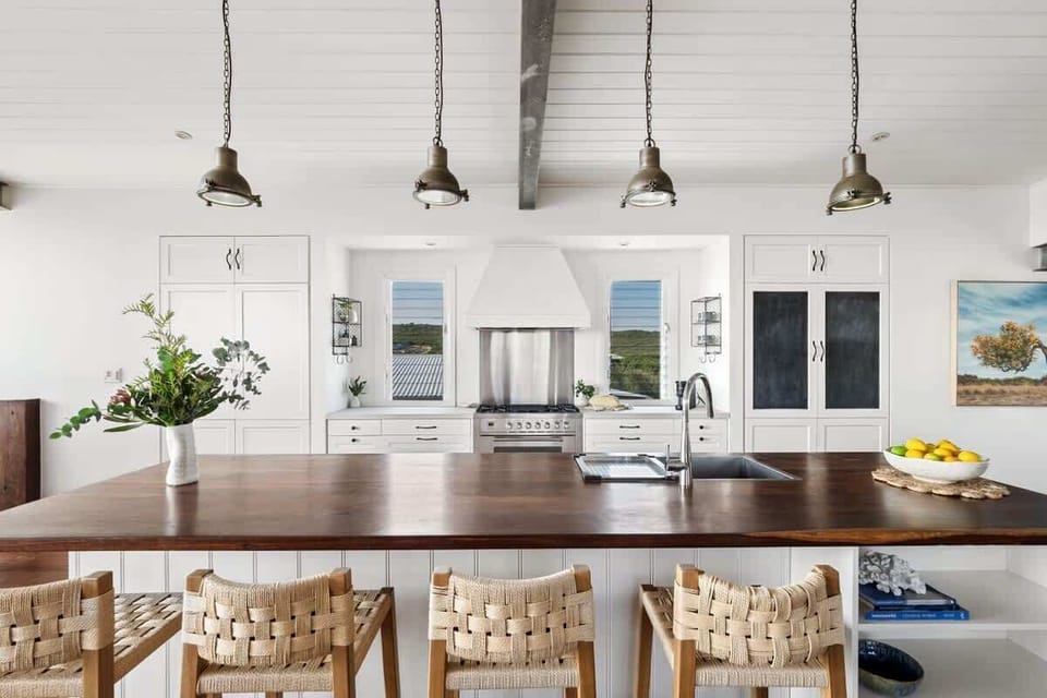Start your mornings gathered around the oversized kitchen island, with woven stools and warm timber finishes adding to the home’s relaxed coastal feel.