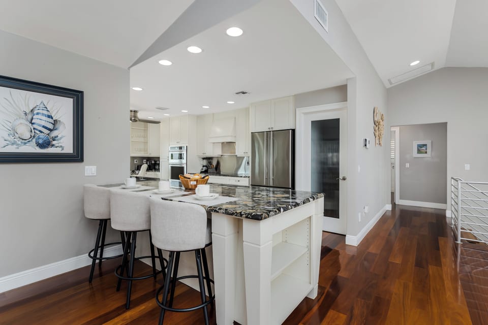 Your gourmet kitchen invites leisurely mornings with its expansive marble island, gleaming stainless appliances, and soaring vaulted ceilings. Warm wood floors guide you through this sunlit open-concept space.