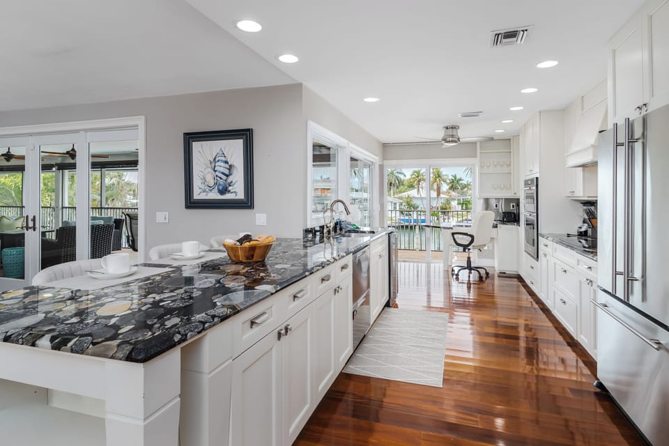 Picture yourself crafting meals in this stunning chef's kitchen, where gleaming marble counters meet warm hardwood floors and sunlight streams through expansive windows framing tropical palm views.