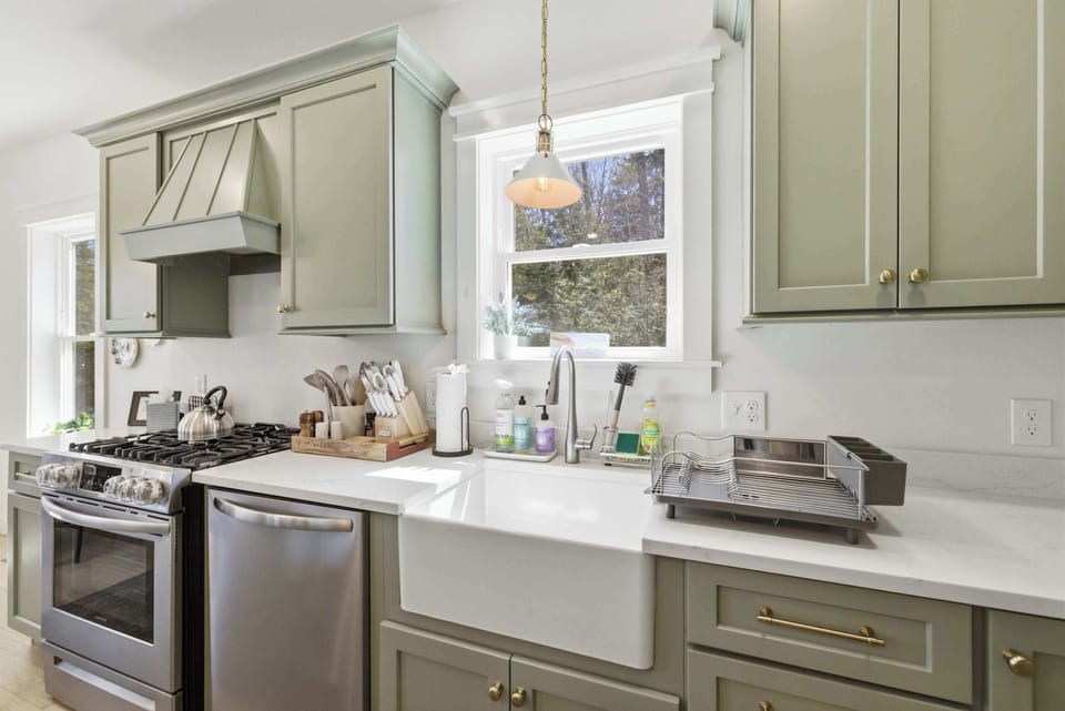 Sage green shaker cabinets, a custom range hood, and a farmhouse sink under the window — every detail in this kitchen was thought through.