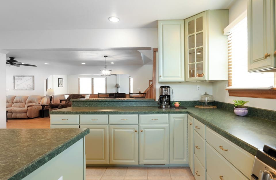 Step into your fully equipped kitchen, where charming green countertops and soft cream cabinets invite you to whip up favorite meals while staying connected to the open living and dining areas.