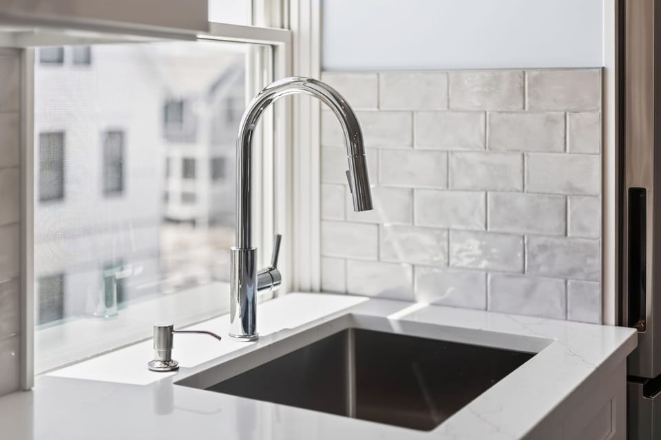 Your bright, modern kitchen features a sleek faucet, crisp white subway tile backsplash, and natural light streaming through the window—perfect for preparing meals in style.