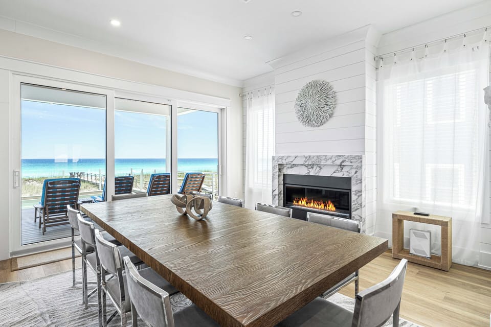 Gather around the expansive dining table with stunning beachfront views through floor-to-ceiling windows. The cozy fireplace and coastal décor create your perfect retreat for memorable meals by the sea.