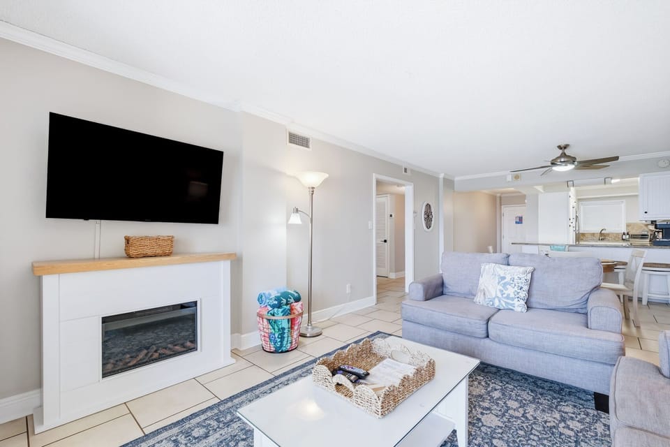 Bright, cozy living room with fireplace, TV, and open kitchen layout