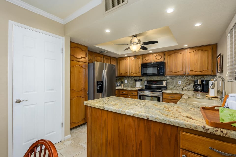 Granite countertops extend over the wooden island and cabinetry beneath a ceiling fan with light.