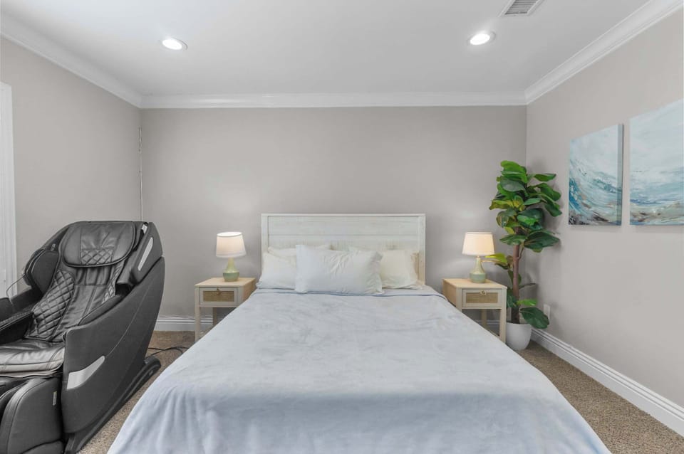 Master bedroom with king bed, massage chair, matching nightstands, and coastal wall art