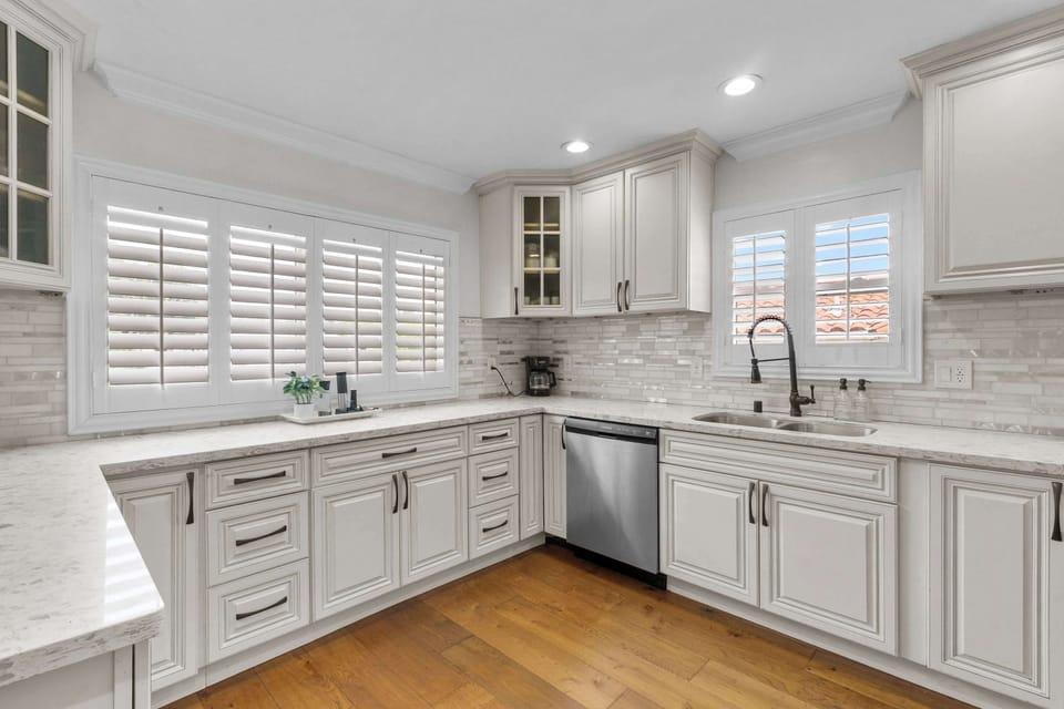 Kitchen with white raised-panel cabinets, quartz countertops, tile backsplash, and stainless steel dishwasher
