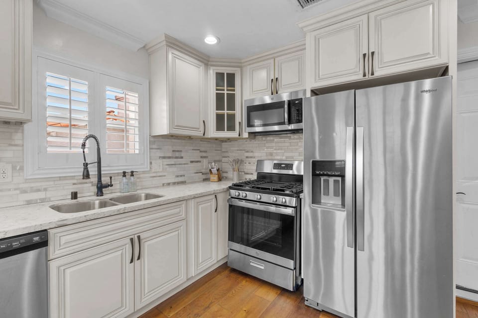 Kitchen with stainless steel gas range, side-by-side refrigerator, microwave, and white cabinets