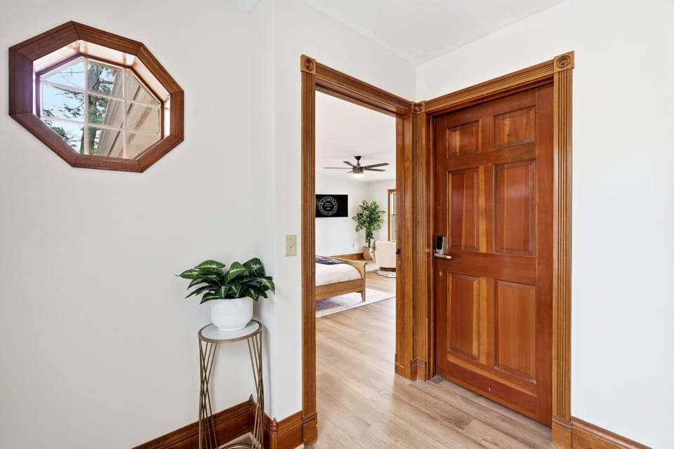 Bright hallway with charming wood trim, a unique window detail, and a welcoming view into the bedroom.