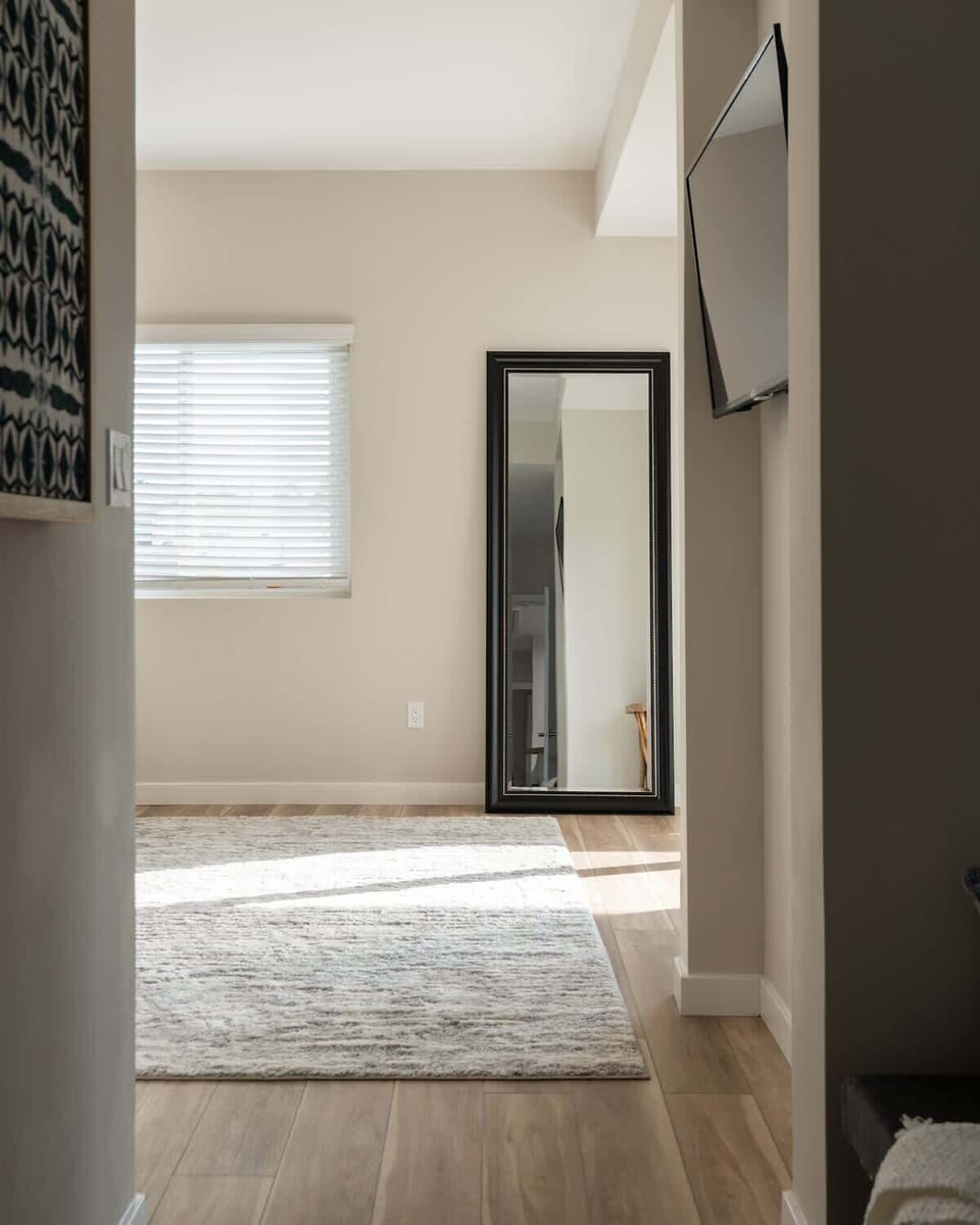The sleek black-framed mirror adds depth and elegance to the space, making it feel more open and bright. The neutral tones and minimalist design create a calming, modern atmosphere. 
