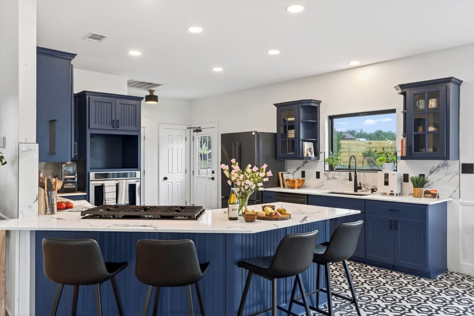 Cook, gather, and entertain in this designer kitchen featuring bold navy cabinetry, marble finishes, and spacious island seating.