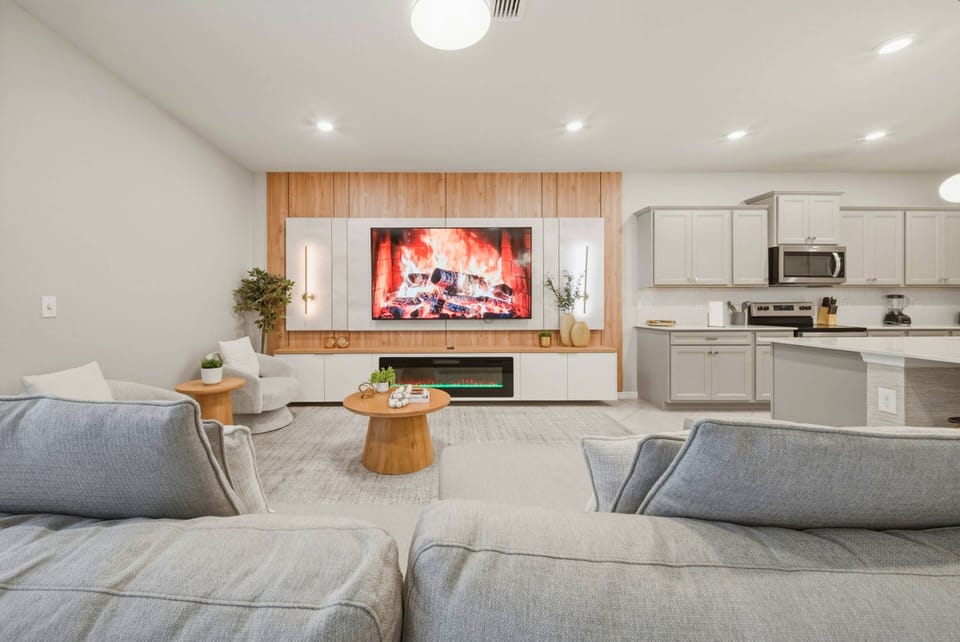 Unwind in the spacious living area with plush gray sofas and a sleek wooden wall that features a cozy fireplace and a large TV, making it an ideal spot for entertainment amidst stylish decor that enhances the modern vibe.
