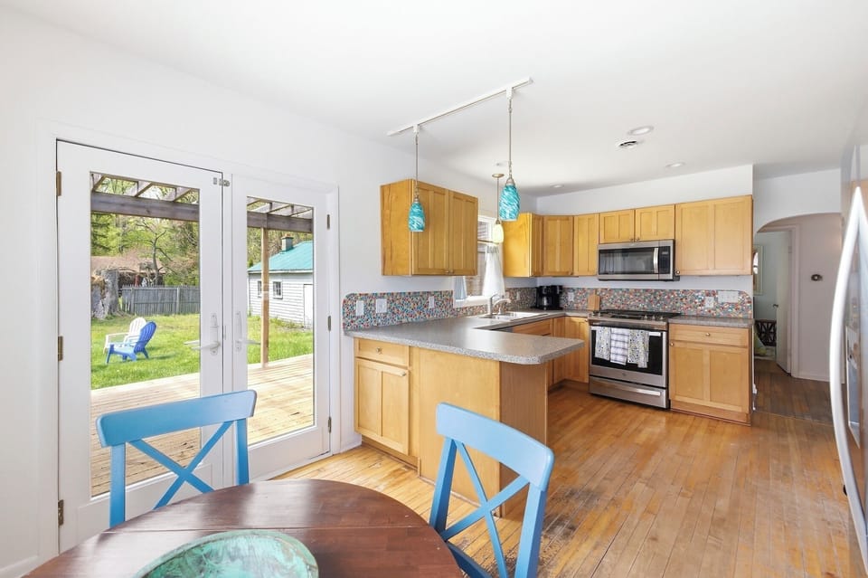 Bright kitchen with wood cabinetry, colorful backsplash, and open layout. Connects to dining area and backyard deck for easy indoor-outdoor living.