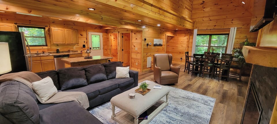 Cozy open-concept cabin living with fireplace, dining area, and full kitchen