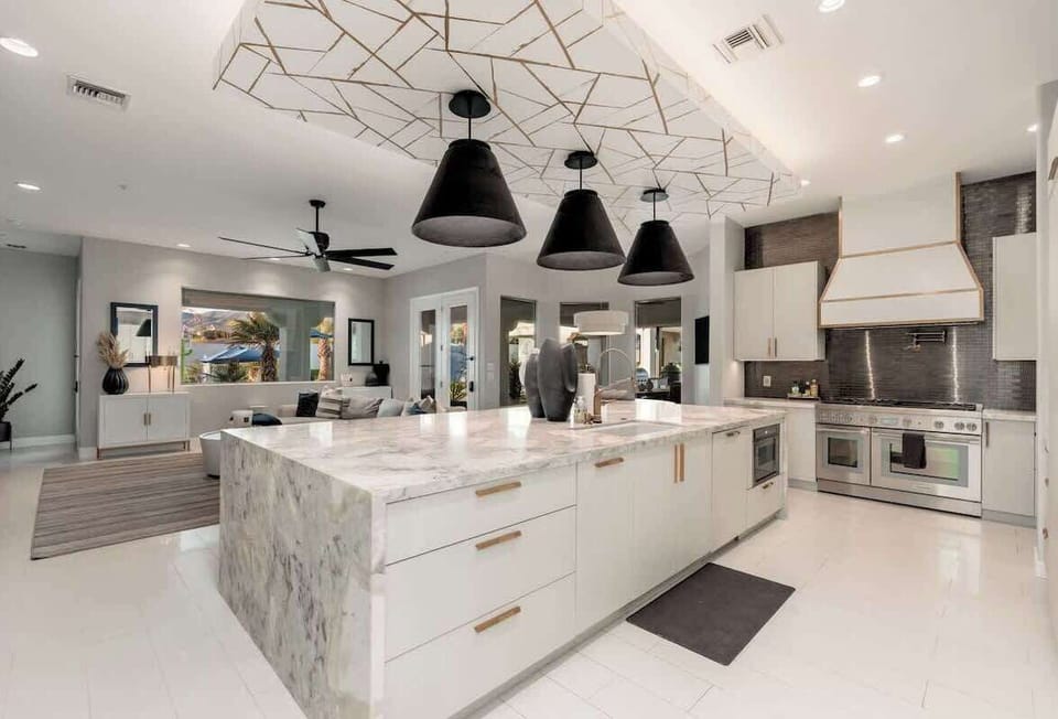 Stunning modern kitchen with marble island, chef-grade appliances, and striking geometric ceiling detail—your culinary dreams come alive in this bright, open space.