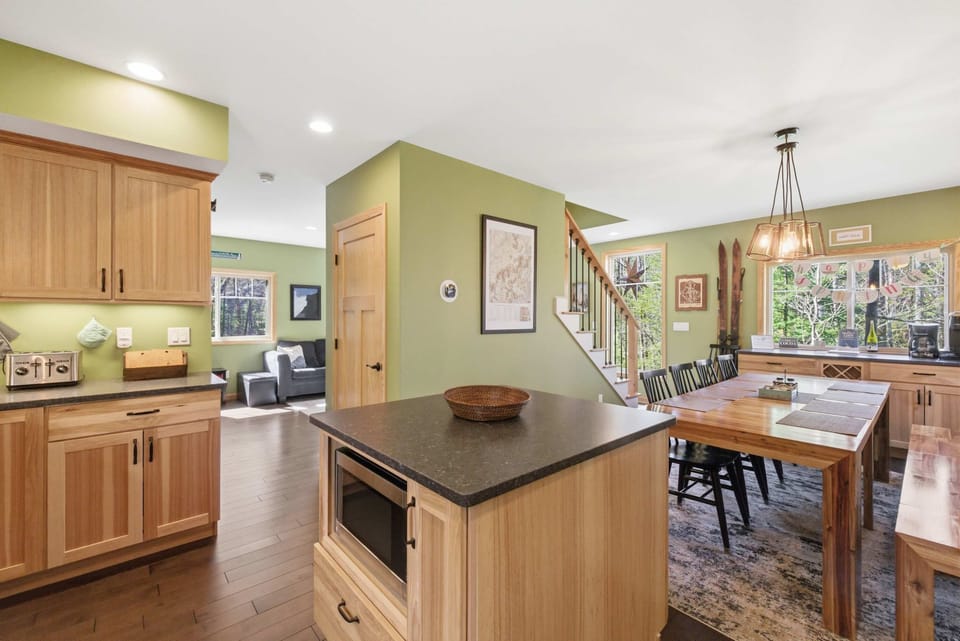 The kitchen and center island from the dining area, looking through toward the farm table and pendant chandelier beyond.