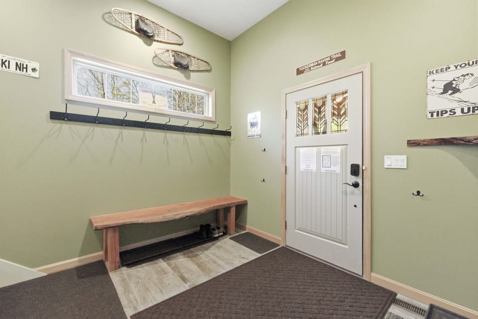 The mudroom's front entry door with live-edge bench, ski-themed signage, and antique snowshoe décor on the walls.