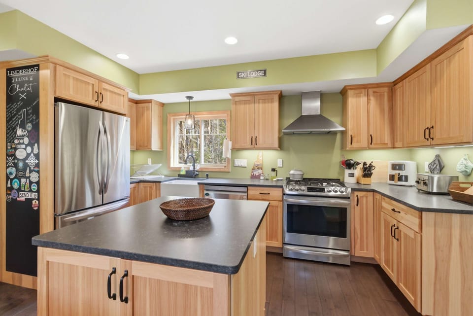 The chef's kitchen with gas range, pro-grade hood, center island, dark countertops, and that sticker-covered fridge.