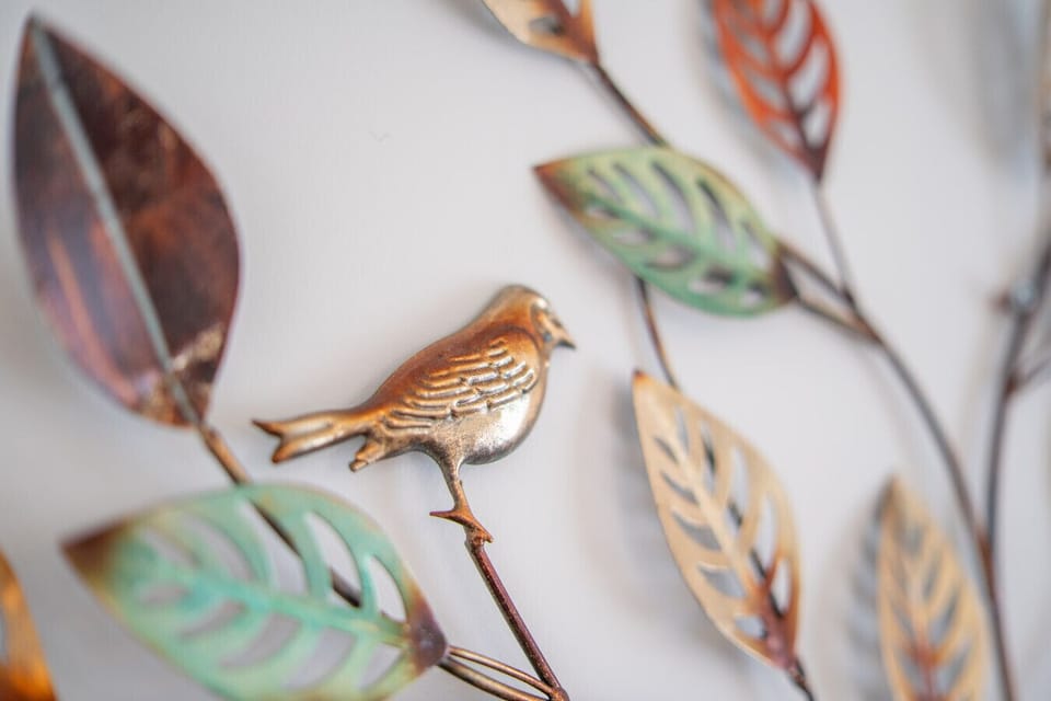 Close-up of a metal bird and leaves on the wall-mounted tree artwork.