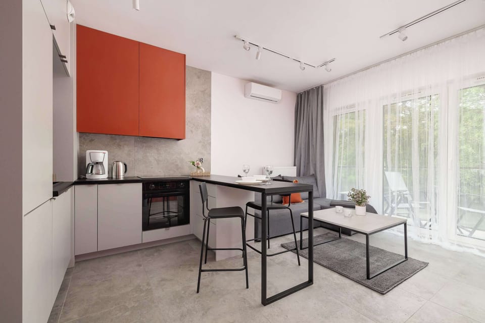 Compact open-plan kitchenette with modern appliances, dining table and stylish orange accents.