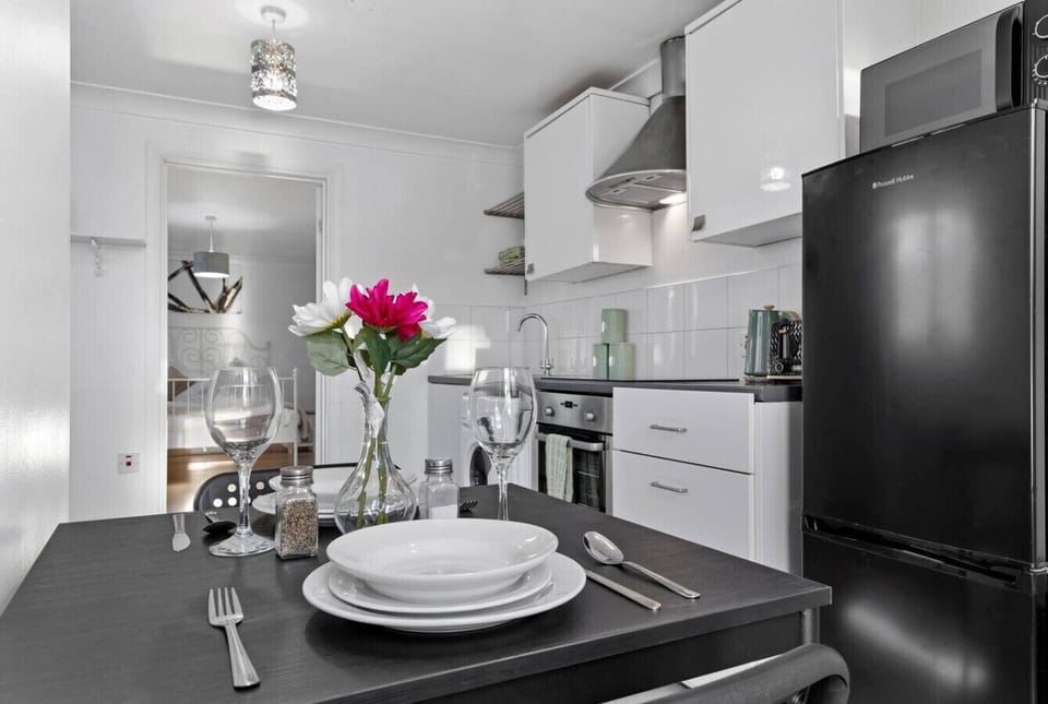 Contemporary kitchenette and dining setup with a set table, wine glasses and flowers, plus a black fridge and modern appliances.