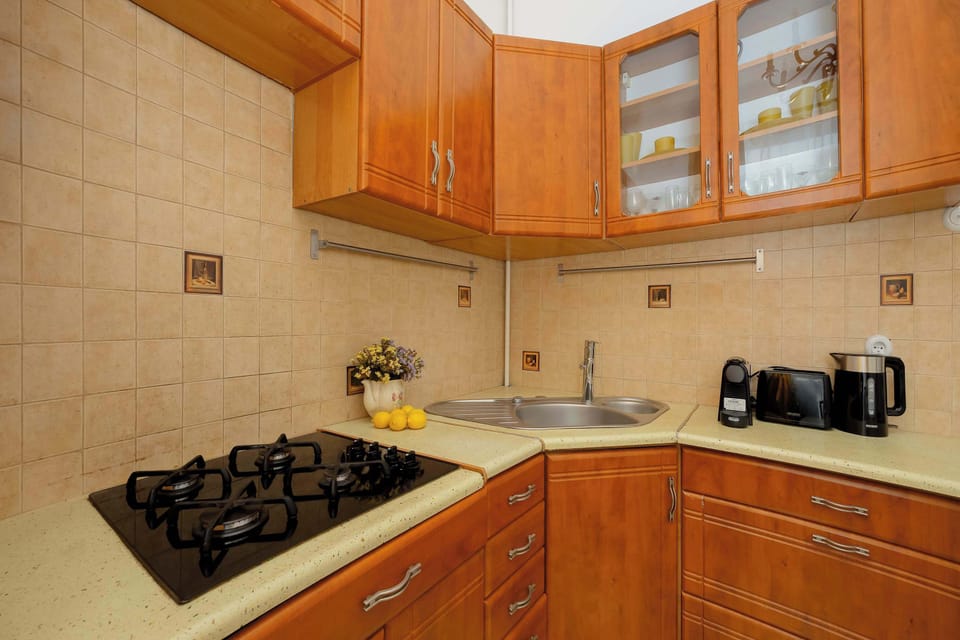 A kitchen corner with a gas stove, tiled walls, and wooden cabinets above.