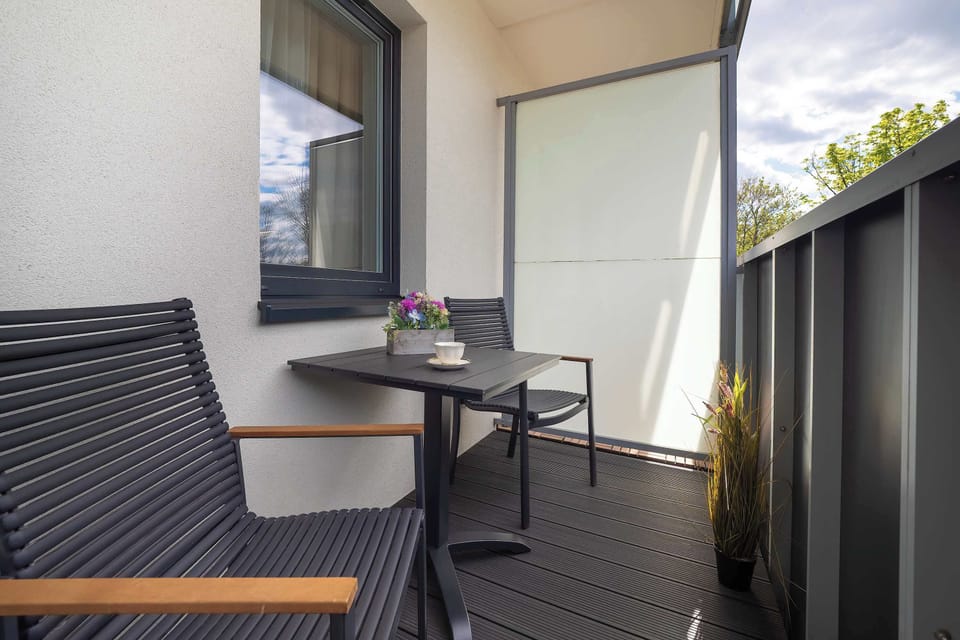 A small balcony with a chair and table, enclosed by dark panels and open to fresh air.