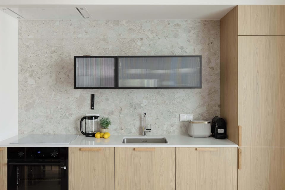 A compact kitchenette with light wood cabinets, a small sink, and built-in appliances.