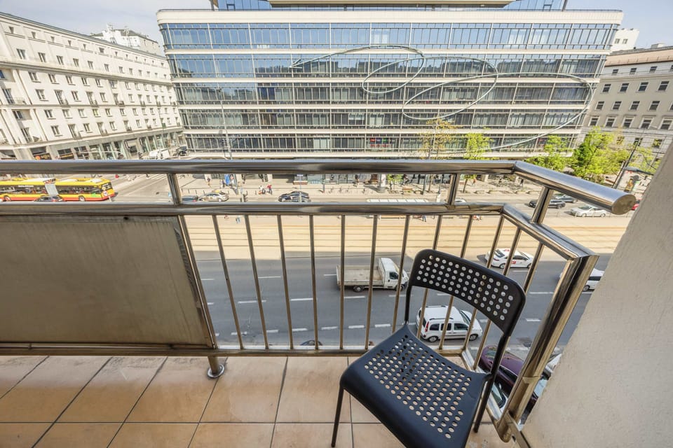 A balcony with outdoor seating overlooking modern buildings and city streets.