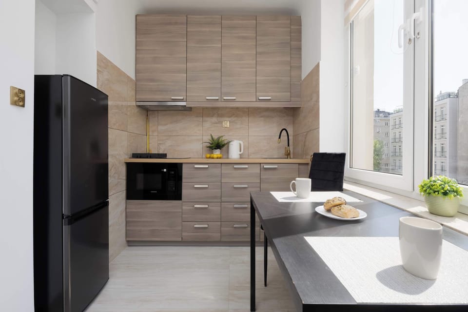 A modern kitchenette with dark appliances, wooden cabinets, and a sleek countertop.