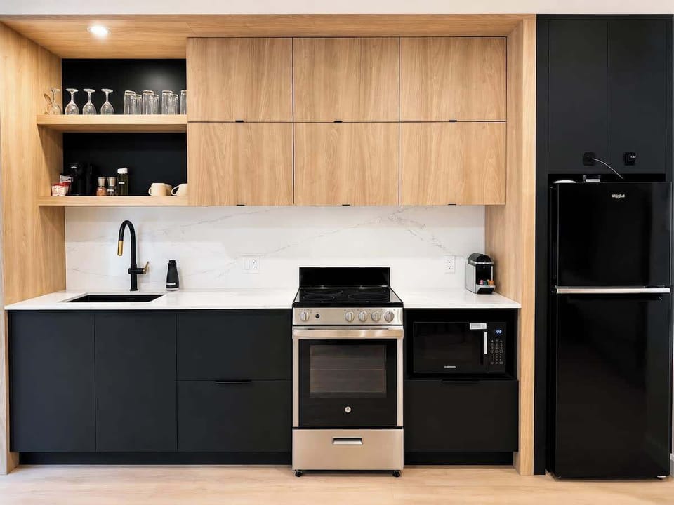 Un bel espace culinaire à aire ouverte doté de lignes épurées, d'un élégant robinet col-de-cygne noir, d'un coin café dédié et d'un grand espace de rangement dissimulé derrière des armoires lisses sans poignées.